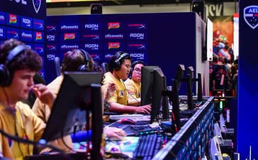 Gamers wearing headsets competing at desktop computers at PAX Aus 2025.