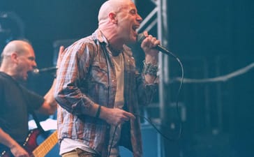 John Bush singing into a handheld microphone during an Armored Saint performance.