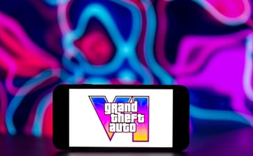 Grand Theft Auto VI logo displayed on a smartphone against a pink and blue neon background.