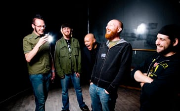 Killswitch Engage members laughing together, with Adam Dutkiewicz at left and Howard Jones in the centre.