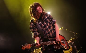 Courtney Barnett leaning forward while playing electric guitar under yellow stage lighting.
