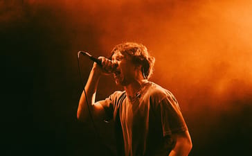 One Step Closer vocalist Ryan Savitski singing into a microphone under orange stage lighting.