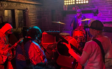 They Are Gutting A Body Of Water performing together under red and purple lighting in a stone-walled venue.