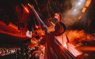 A giant TSIM puppet towers over the stage under orange lights.