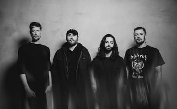 After The Burial’s four members standing against a plain wall in a black-and-white publicity photograph.