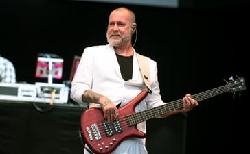 Limp Bizkit bassist Sam Rivers plays a red bass while wearing a white suit at Leeds Festival in 2025.