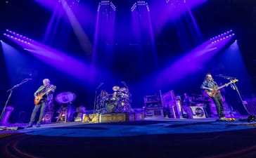 Alex Lifeson, Anika Nilles and Geddy Lee perform on a stage lit blue and purple in Fort Worth.