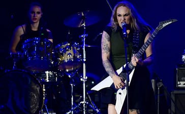 Nervosa's Prika Amaral sings into a microphone while playing a white guitar at Rock in Rio.