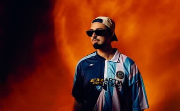 Sonny Fodera wearing sunglasses and a backwards cap against an orange background.