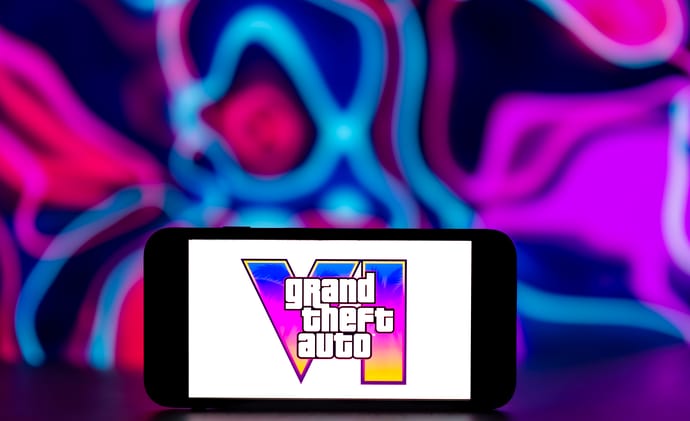 Grand Theft Auto VI logo displayed on a smartphone against a pink and blue neon background.