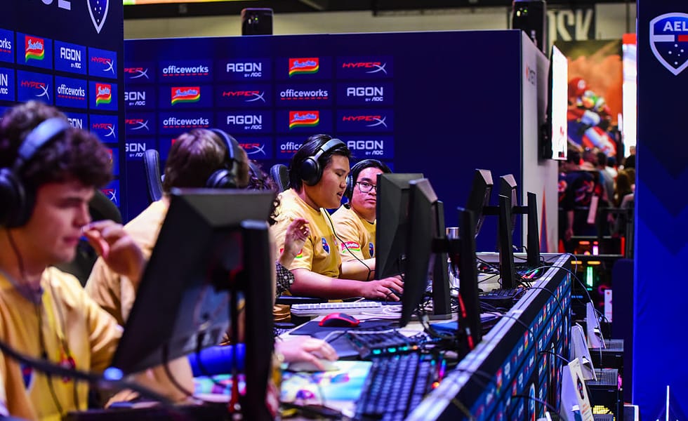 Gamers wearing headsets competing at desktop computers at PAX Aus 2025.