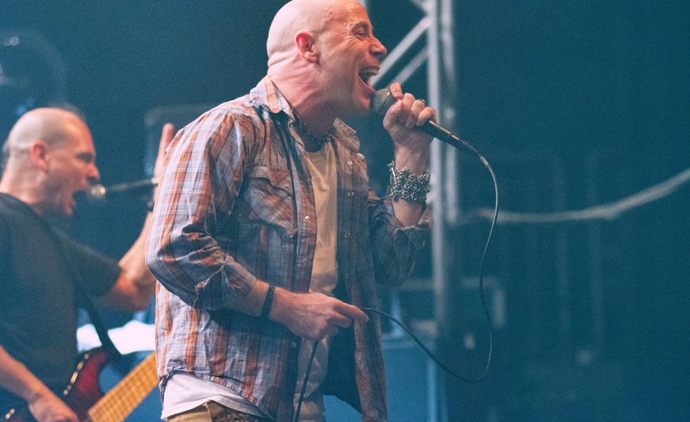 John Bush singing into a handheld microphone during an Armored Saint performance.