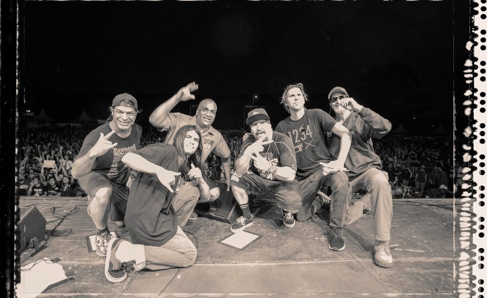 Black-and-white group photograph of Infectious Grooves posing on stage, with a crowd behind them.