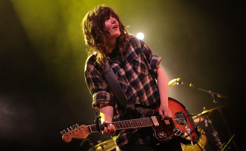 Courtney Barnett leaning forward while playing electric guitar under yellow stage lighting.