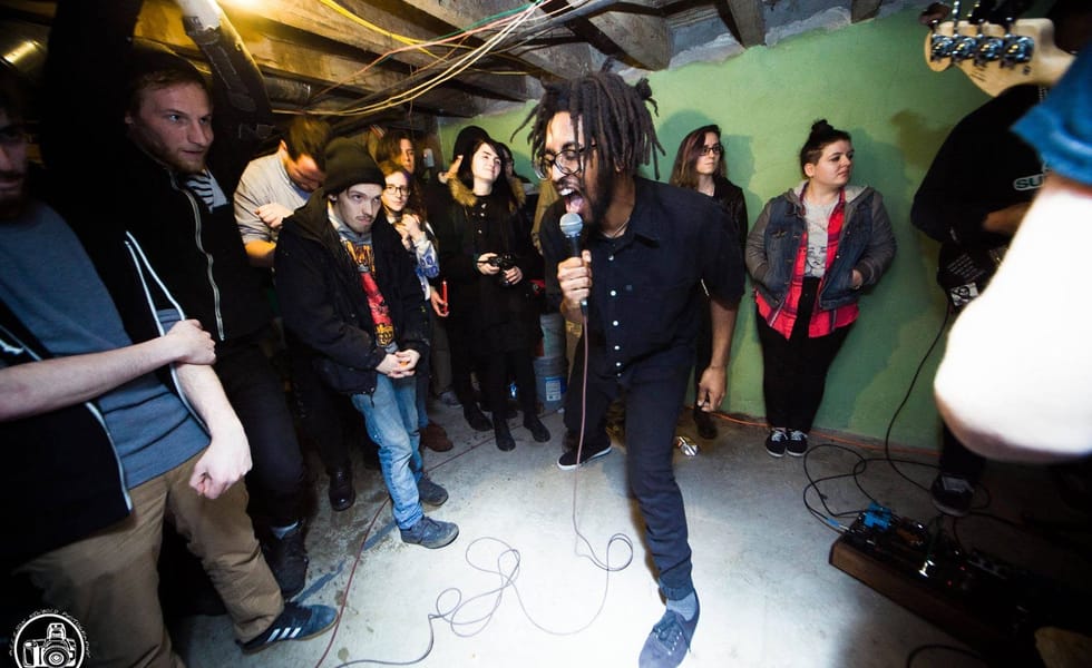 Soul Glo vocalist Pierce Jordan singing into a microphone, surrounded by fans at a basement show.