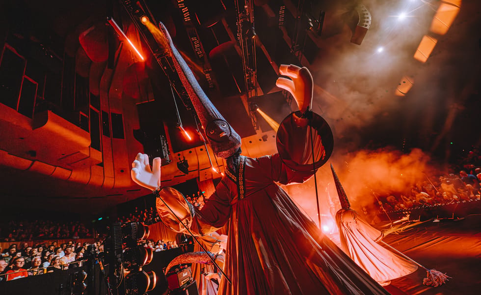 A giant TSIM puppet towers over the stage under orange lights.