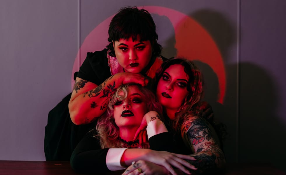 Three members of Vipersnatch pose together under red lighting against a grey wall.