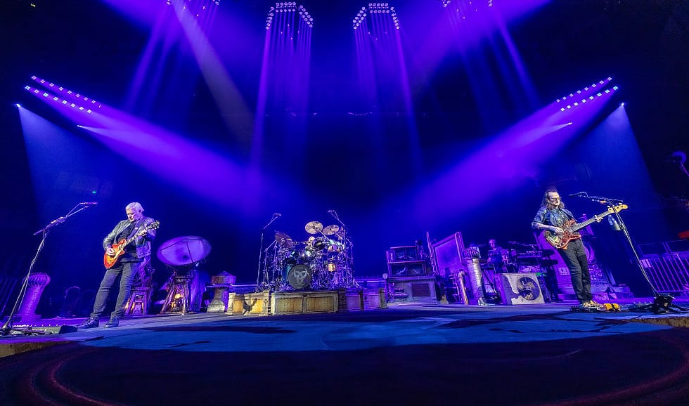 Alex Lifeson, Anika Nilles and Geddy Lee perform on a stage lit blue and purple in Fort Worth.