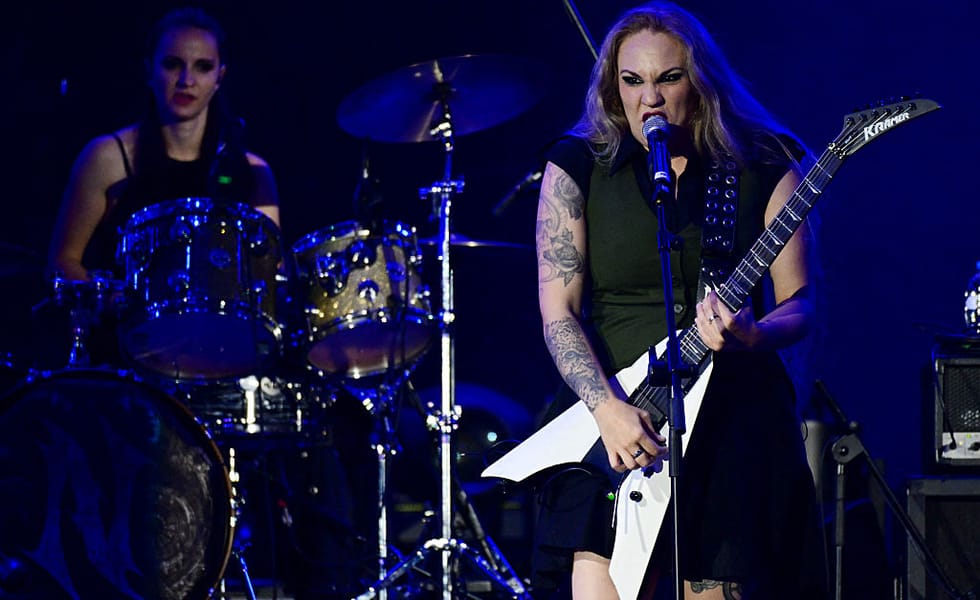Nervosa's Prika Amaral sings into a microphone while playing a white guitar at Rock in Rio.